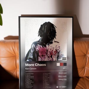 Op de afbeelding: Een ingelijste albumkunstprint voor "More Chaos" van Ken Carson. De afbeelding toont een figuur met zwarte dreadlocks, bespat met rode en witte verf. De albumtitel en tracklist worden in witte tekst op een donkere achtergrond weergegeven.