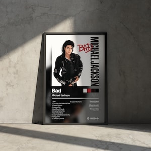 May include: Framed poster featuring Michael Jackson's album "Bad." The image shows Jackson in a black jacket. The poster includes the album title, tracklist, and artist's name in white and red text against a black background. The poster is displayed against a gray wall.