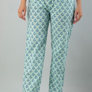 May include: Light blue pants with a repeating blue floral pattern. The pants are a relaxed fit and appear to be made of a lightweight fabric. The pants are worn with clear strap heels.