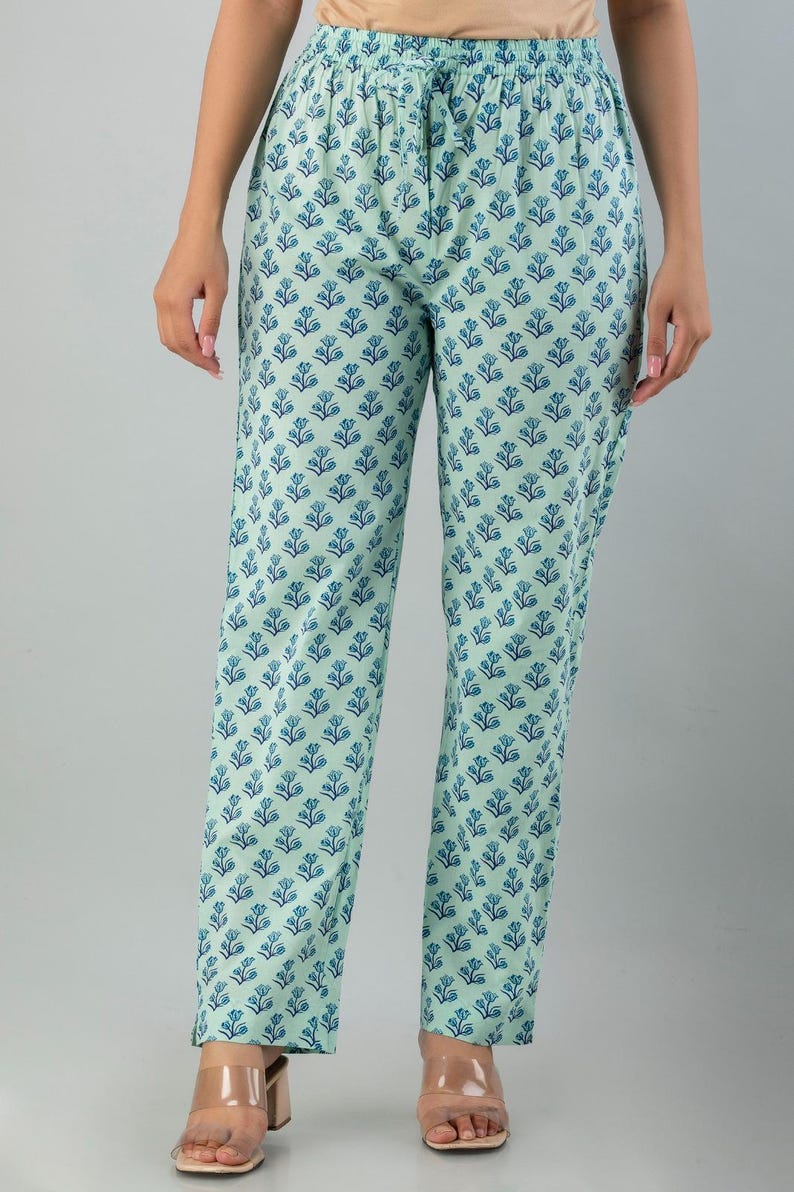 May include: Light blue pants with a repeating blue floral pattern. The pants are a relaxed fit and appear to be made of a lightweight fabric. The pants are worn with clear strap heels.
