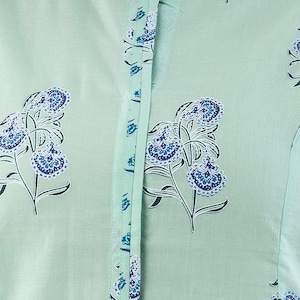 May include: A close-up of a light green button-down shirt with a floral pattern in dark and light blue. The shirt has a mandarin collar and a vertical line of buttons down the front. The floral design is repeated across the fabric.