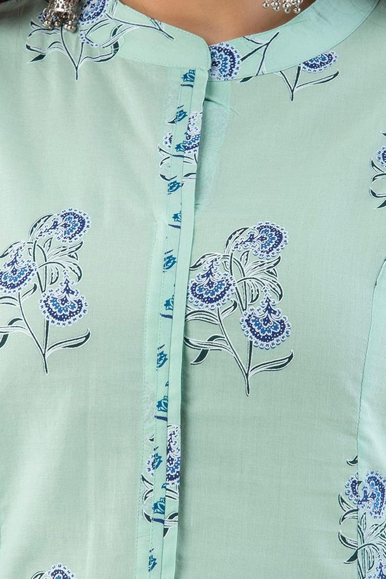 May include: A close-up of a light green button-down shirt with a floral pattern in dark and light blue. The shirt has a mandarin collar and a vertical line of buttons down the front. The floral design is repeated across the fabric.