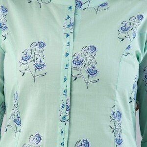 May include: A light green tunic with a mandarin collar and long sleeves. The tunic is decorated with a repeating floral pattern in shades of blue and white. The button placket and collar are trimmed with a blue floral design.