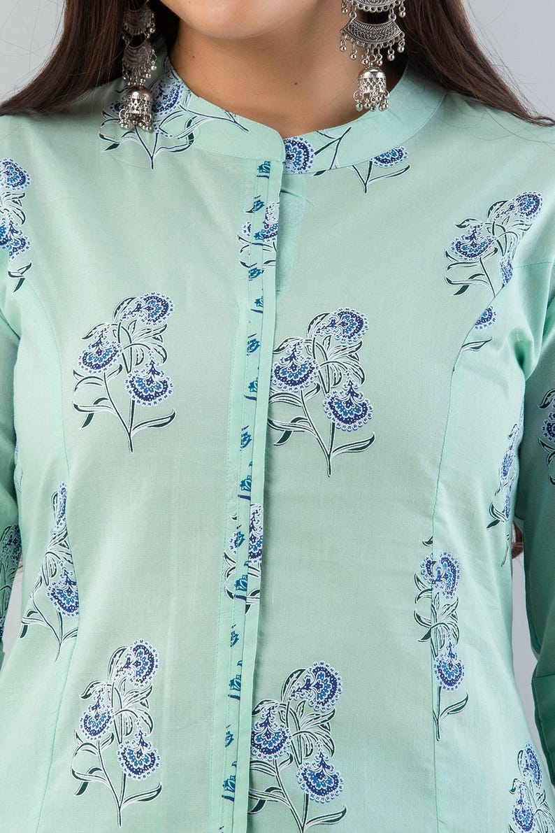 May include: A light green tunic with a mandarin collar and long sleeves. The tunic is decorated with a repeating floral pattern in shades of blue and white. The button placket and collar are trimmed with a blue floral design.