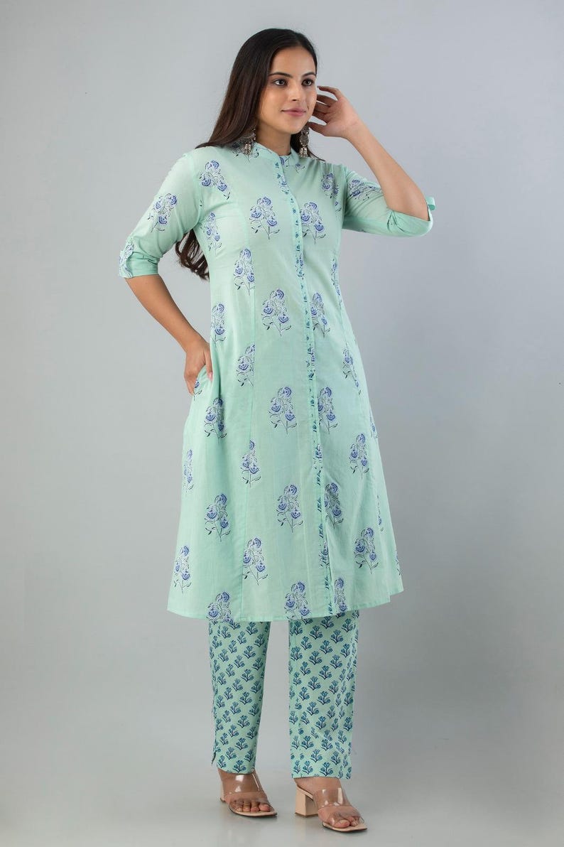 May include: A mint green two-piece outfit featuring a long-sleeved tunic and matching pants. The tunic has a mandarin collar and a button-down front. Both pieces are adorned with a blue floral pattern. The outfit is made of a lightweight fabric.