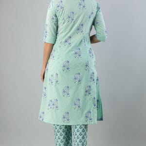 May include: A mint green two-piece outfit featuring a tunic top and matching pants. The ensemble is adorned with a repeating blue floral pattern. The tunic has a mandarin collar and three-quarter sleeves. The pants are straight-legged.