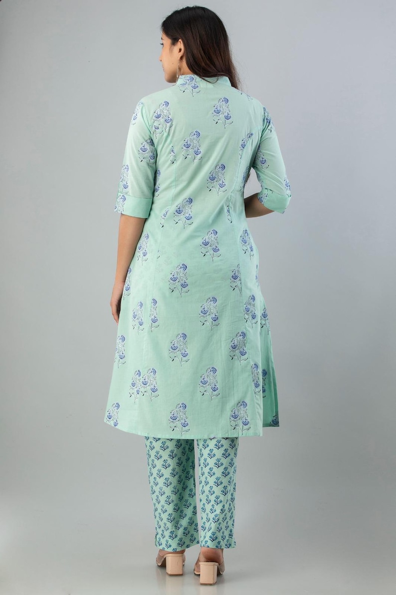 May include: A mint green two-piece outfit featuring a tunic top and matching pants. The ensemble is adorned with a repeating blue floral pattern. The tunic has a mandarin collar and three-quarter sleeves. The pants are straight-legged.