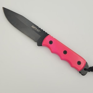 May include: A black MTech USA knife with a vibrant pink handle. The blade is black, and the handle is secured with three black screws. A black lanyard is attached to the handle's end.