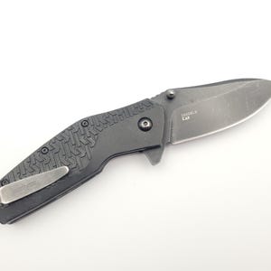 Op de afbeelding: Een zwart vouwmes met een getextureerde handgreep en een zilverkleurig lemmet. Het mes heeft een zakclip en de tekst "Kershaw" is zichtbaar. Op het lemmet staat de tekst "3550BLK CA".
