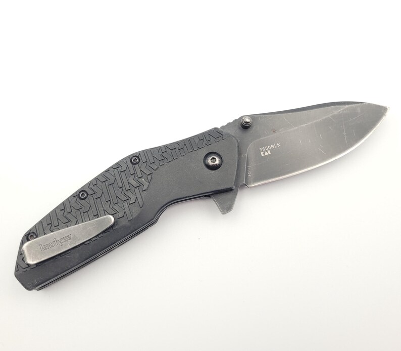 Op de afbeelding: Een zwart vouwmes met een getextureerde handgreep en een zilverkleurig lemmet. Het mes heeft een zakclip en de tekst "Kershaw" is zichtbaar. Op het lemmet staat de tekst "3550BLK CA".