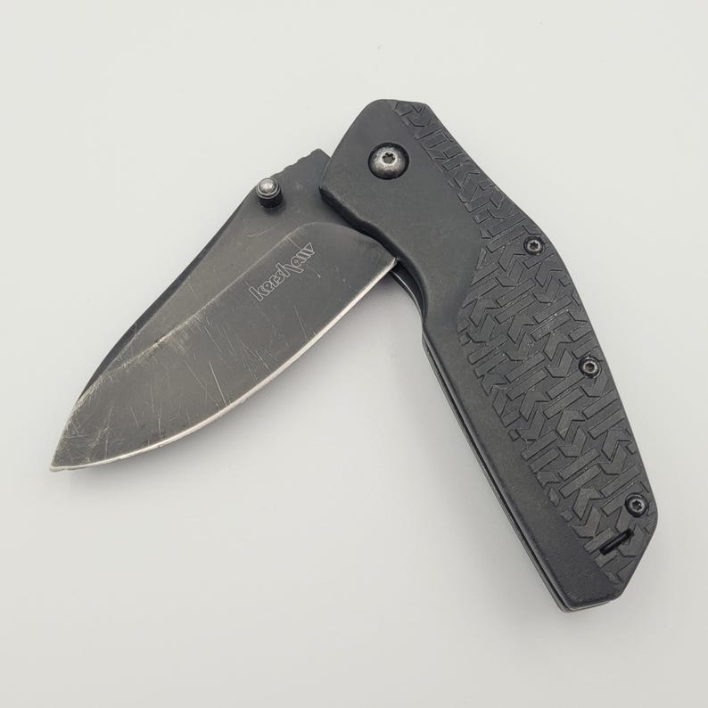 Op de afbeelding: Een zwart vouwmes met een gedeeltelijk open lemmet. Het lemmet heeft een donkere afwerking en de handgreep heeft een gestructureerd patroon. Het mes is een praktisch hulpmiddel voor diverse taken.