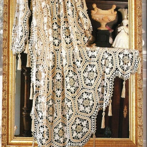 Puede incluir: Un mantel de crochet blanco con un patrón geométrico y borlas cuelga en un marco dorado. El mantel está drapeado sobre una superficie de madera y tiene un diseño delicado e intrincado.