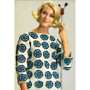 May include: A white crocheted sweater with a blue floral pattern. The sweater has a round neckline and three-quarter sleeves.