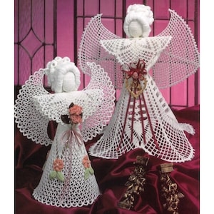 May include: Two white crocheted angel ornaments with lace detailing and pink rose accents. The larger angel has a red ribbon and a heart-shaped design on its dress. The smaller angel has a pink ribbon and a bow.