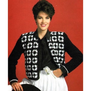 May include: A black crocheted jacket with white crocheted squares on the front and sleeves. The jacket has a collar and long sleeves.