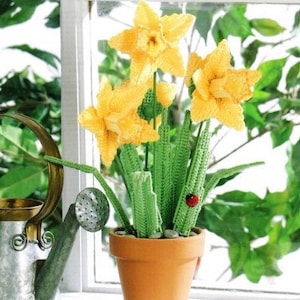 Könnte beinhalten: Eine gehäkelte Narzissenpflanze in einem Terrakotta-Topf. Die Pflanze hat gelbe Blüten und grüne Blätter. Auf einem der Blätter sitzt ein Marienkäfer.