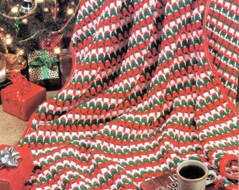 May include: A red, white, and green crocheted blanket with a teddy bear sitting on top of it. The blanket is made with a textured stitch and has a scalloped edge. There is a book with the text "10 TRAD'L CHRIST." and a cup of coffee on the blanket.