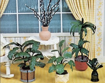 May include: Miniature potted plants in various styles, including a palm tree and leafy plants in a wooden barrel pot and woven basket. A vase with black branches and white buds sits on a small table. The scene is set in front of a window.