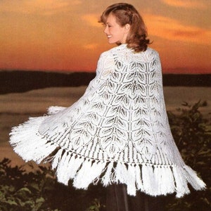 May include: A white crocheted shawl with a leaf pattern and fringe. The shawl is draped over a person's shoulders and the background is a sunset.