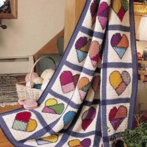 Puede incluir: Una manta de ganchillo con un diseño de patchwork de corazones coloridos. La manta está hecha con hilo blanco y azul y presenta una variedad de colores, incluyendo rojo, rosa, morado, verde, amarillo y naranja.