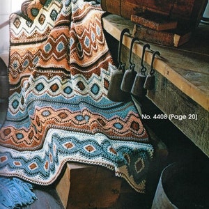 Puede incluir: Una colorida manta de ganchillo hecha a mano con patrones geométricos en tonos marrones, azules y melocotón. La manta está sobre una superficie de madera, con el texto "No. 4408 (Página 20)" visible.