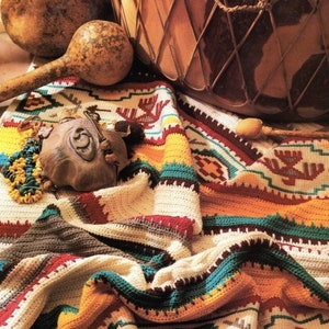Puede incluir: Una manta de crochet colorida con patrones geom&eacute;tricos en tonos de rojo, naranja, amarillo, verde, azul y marr&oacute;n. La manta est&aacute; drapeada sobre un tambor de madera y un sonajero de calabaza.