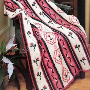 May include: A crocheted throw blanket with a pink, white, and black striped pattern. The blanket features a repeating rose design and is draped over a chair.