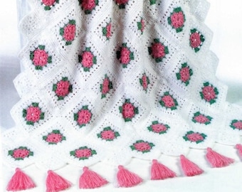 May include: A white crocheted blanket with pink and green flower designs and pink tassels along the bottom edge.