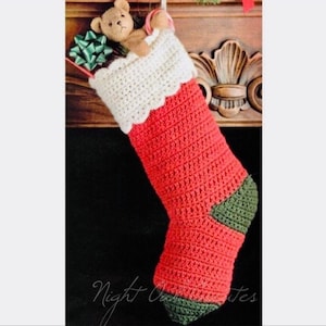 May include: A crocheted Christmas stocking with a white crocheted cuff, red body, and green toe. The stocking is filled with a small teddy bear and a green gift box.