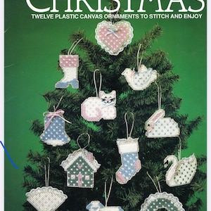 May include: Twelve plastic canvas ornaments to stitch and enjoy. The ornaments feature a variety of Victorian Christmas themes, including a heart, a boot, a bird, a cat, a bell, a rabbit, a stocking, a swan, a house, a doily, a lamb, and a wreath. The ornaments are all white with pink and blue accents.