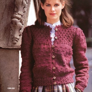 May include: A maroon knitted cardigan with a button-up front and a delicate lace pattern on the neckline and cuffs. The cardigan is worn over a white collared shirt and a plaid skirt.