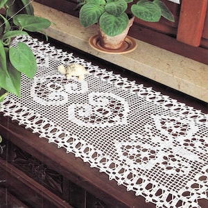 May include: White crocheted table runner with a delicate lace pattern and a small decorative turtle figurine on top.