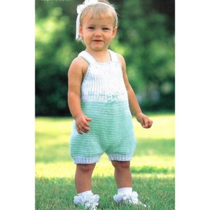 May include: A baby girl wearing a light green and white crocheted romper. The romper has a white crocheted top and a light green crocheted bottom. The baby is standing on a grassy lawn.