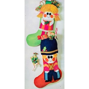 May include: Two Christmas stockings with a girl and a toy soldier design. The girl stocking is green with a pink and white striped dress and yellow yarn hair. The toy soldier stocking is red with a blue hat and a pink and yellow uniform.
