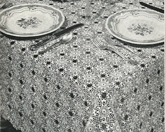 May include: A white crocheted tablecloth with a delicate floral pattern. The tablecloth is laid out on a table with two plates, silverware, and a glass.