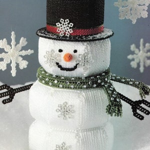 May include: A white snowman with a black top hat, red ribbon, and green scarf decorated with white snowflakes. The snowman has a carrot nose and a smiling face.