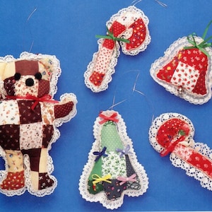 May include: A collection of handmade fabric Christmas ornaments. The ornaments include a teddy bear, a bell, a Christmas tree, and two candy canes. Each ornament is made of patchwork fabric and trimmed with white lace and red bows.