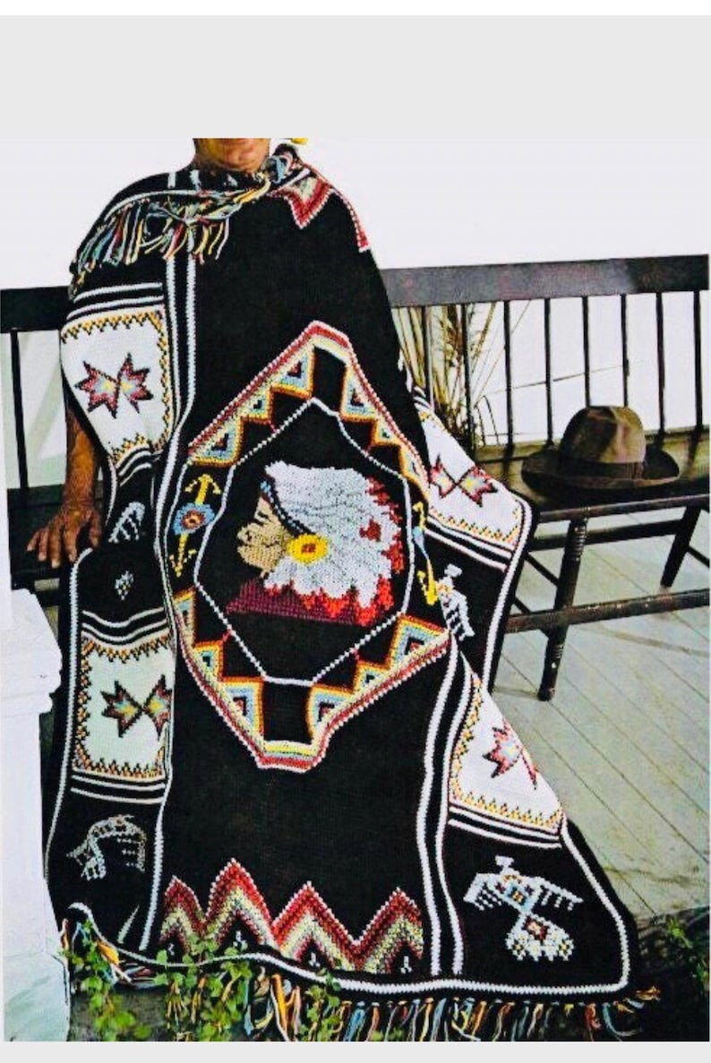 May include: A black crochet blanket with a colorful Native American design featuring a beaded profile of a person wearing a headdress. The blanket has fringe on the bottom and is draped over a wooden bench.