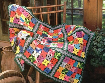 Op de afbeelding: Een kleurrijk gehaakt deken met een bloemenpatroon in tinten roze, blauw, groen, geel en rood. Het deken is over een houten stoel gelegd.