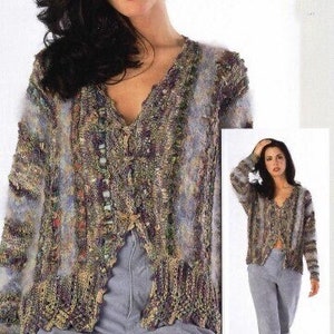 May include: A multi-coloured, open-front cardigan with a V-neck and button closure. The sweater features a textured knit design with shades of brown, purple, and blue. The model is wearing grey trousers. The image also includes a smaller inset image of the same cardigan.