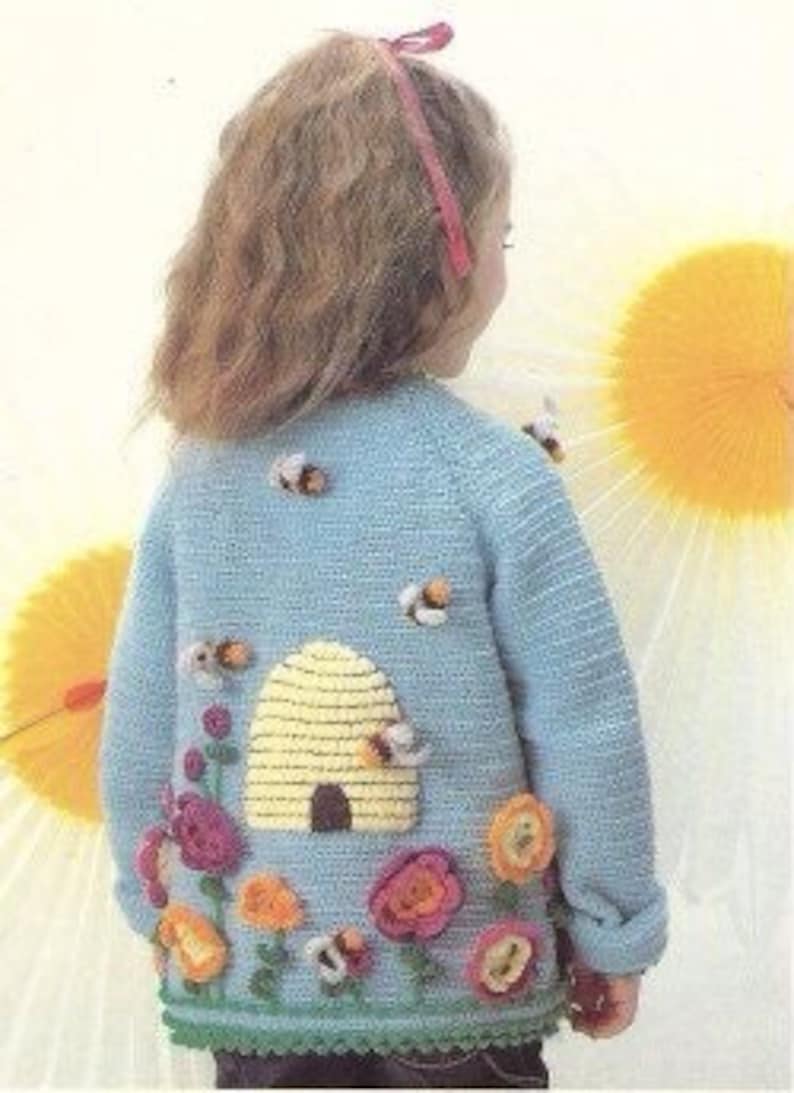 Puede incluir: Un c&aacute;rdigan de punto azul claro con una colmena y abejas bordadas en la espalda. La colmena es amarilla y tiene una peque&ntilde;a puerta marr&oacute;n. Tambi&eacute;n hay varias flores rosas, naranjas y amarillas bordadas en la espalda.