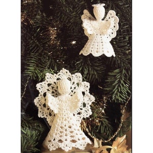 May include: Two white crocheted angel ornaments hanging on a green Christmas tree. The angels have delicate lace details and are a traditional holiday decoration.