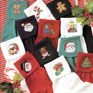 Pode incluir: Uma coleção de meias de Natal com vários desenhos bordados em ponto cruz. Os desenhos incluem uma rena, um bastão de doces, um homem de gengibre, o Pai Natal, um comboio, um anjo, um cão, um soldado de brinquedo, um boneco de neve, um urso numa meia e uma árvore de Natal.