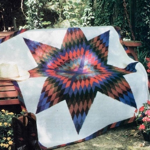 May include: A white crochet blanket with a large, colorful star design in shades of red, blue, green, and brown. The blanket is draped over a wooden bench.