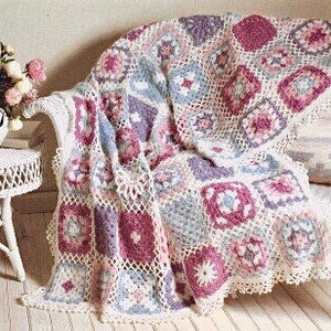 May include: A crocheted throw blanket with a patchwork design featuring squares in shades of purple, pink, and blue. The blanket is made with a white yarn and has a delicate crocheted border.