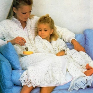 May include: A white crocheted robe with a lacy trim. The robe is worn by a woman and a young girl. The woman is holding a spoon and a small bowl.