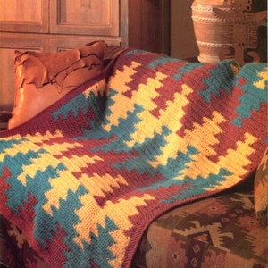 May include: A crocheted throw blanket with a Southwestern-inspired geometric pattern in shades of teal, yellow, and brown. The blanket is draped over a couch with a patterned fabric.