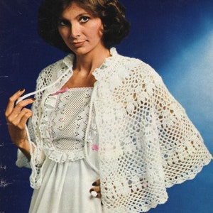 Puede incluir: Un chal blanco de ganchillo con un delicado patrón floral. El chal se lleva sobre un vestido blanco con ribetes de encaje.