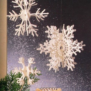May include: Three white, decorative snowflakes of varying sizes hang against a dark background. The snowflakes have intricate, delicate designs, resembling real snowflakes. The image suggests a winter or holiday theme, suitable for seasonal decor.