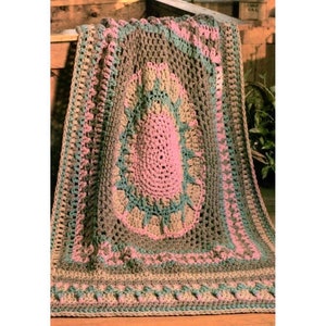 May include: A crocheted throw blanket with a large oval center in pink, surrounded by a border in shades of brown, green, and pink. The blanket has a fringed edge.